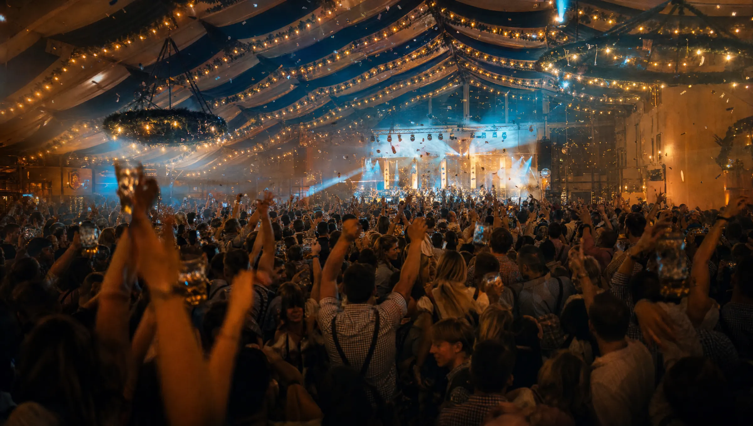 Volles Festzelt bei Nacht mit Bühnenlicht und erhobenen Maßkrügen
